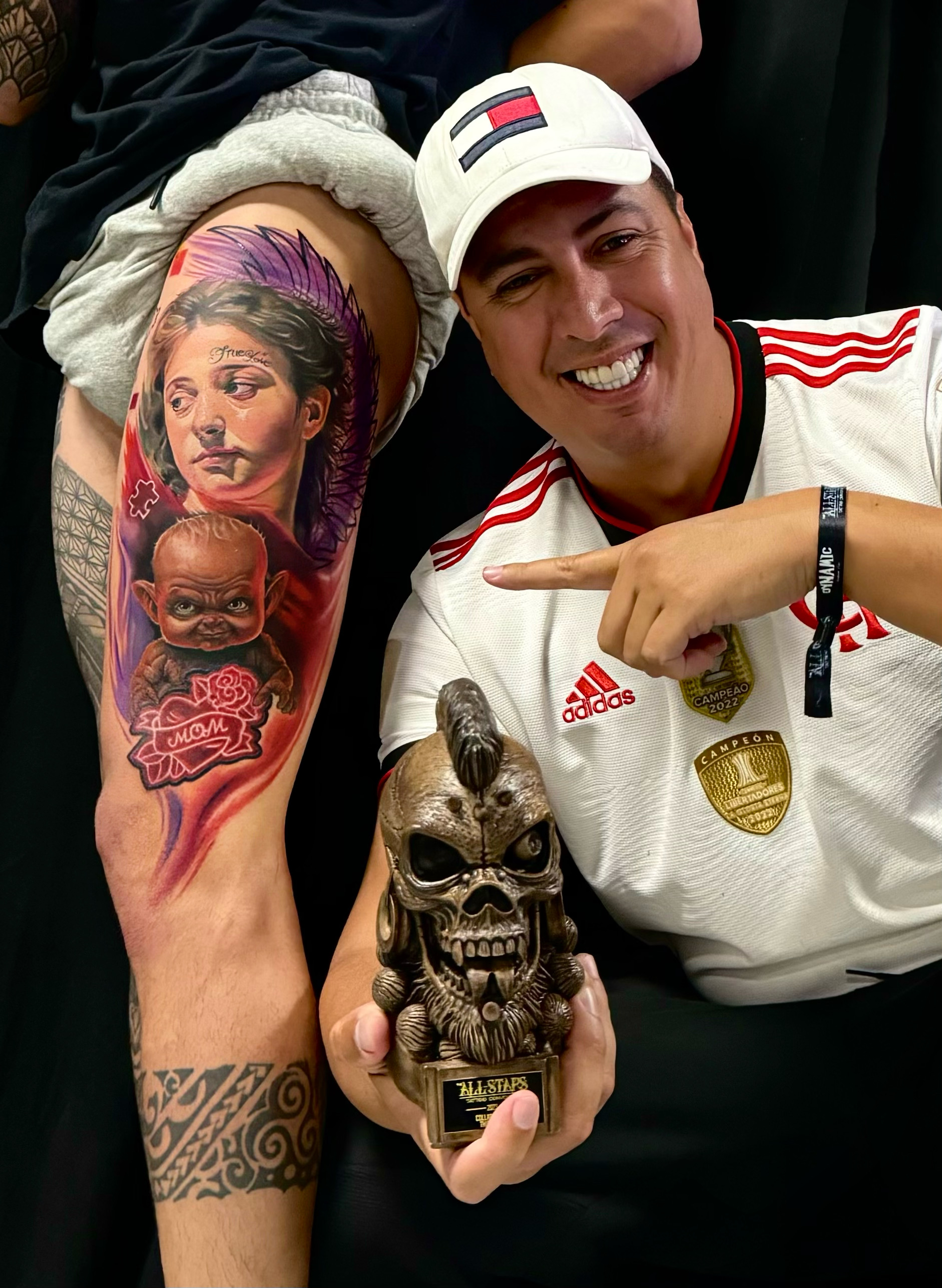 Gustavo premiado, apontando para a tatuagem e o troféu